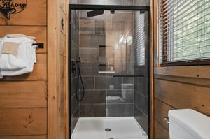 Step into your modern glass shower with sleek dark tiles and rainfall showerhead, perfectly complementing the warm wood cabin atmosphere.
