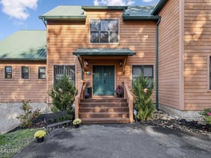 Cedarclad exterior features a welcoming entrance with teal double doors, framed by planters and a covered entryway. The property offers convenient parking and showcases its distinctive green metal ro