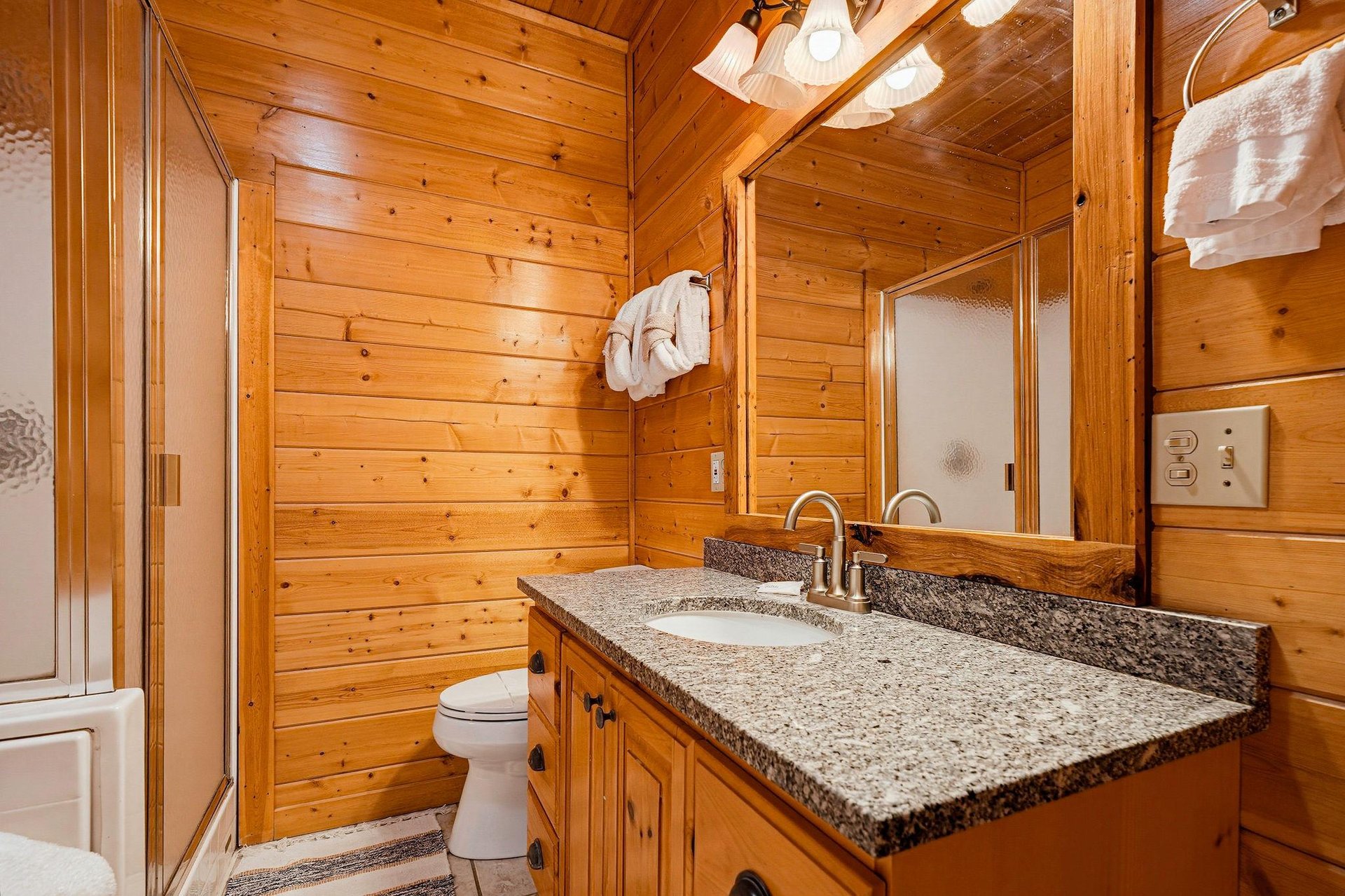 Step into your private bathroom, where warm wood paneling creates a cozy cabin feel. Fresh towels await, and the granite vanity offers plenty of space to settle in.
