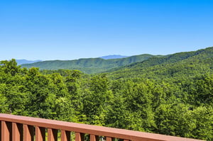 Sweeping mountain views stretch across lush, forested ridges under a bright blue sky. The scenic overlook offers a peaceful glimpse of the surrounding natural landscape.