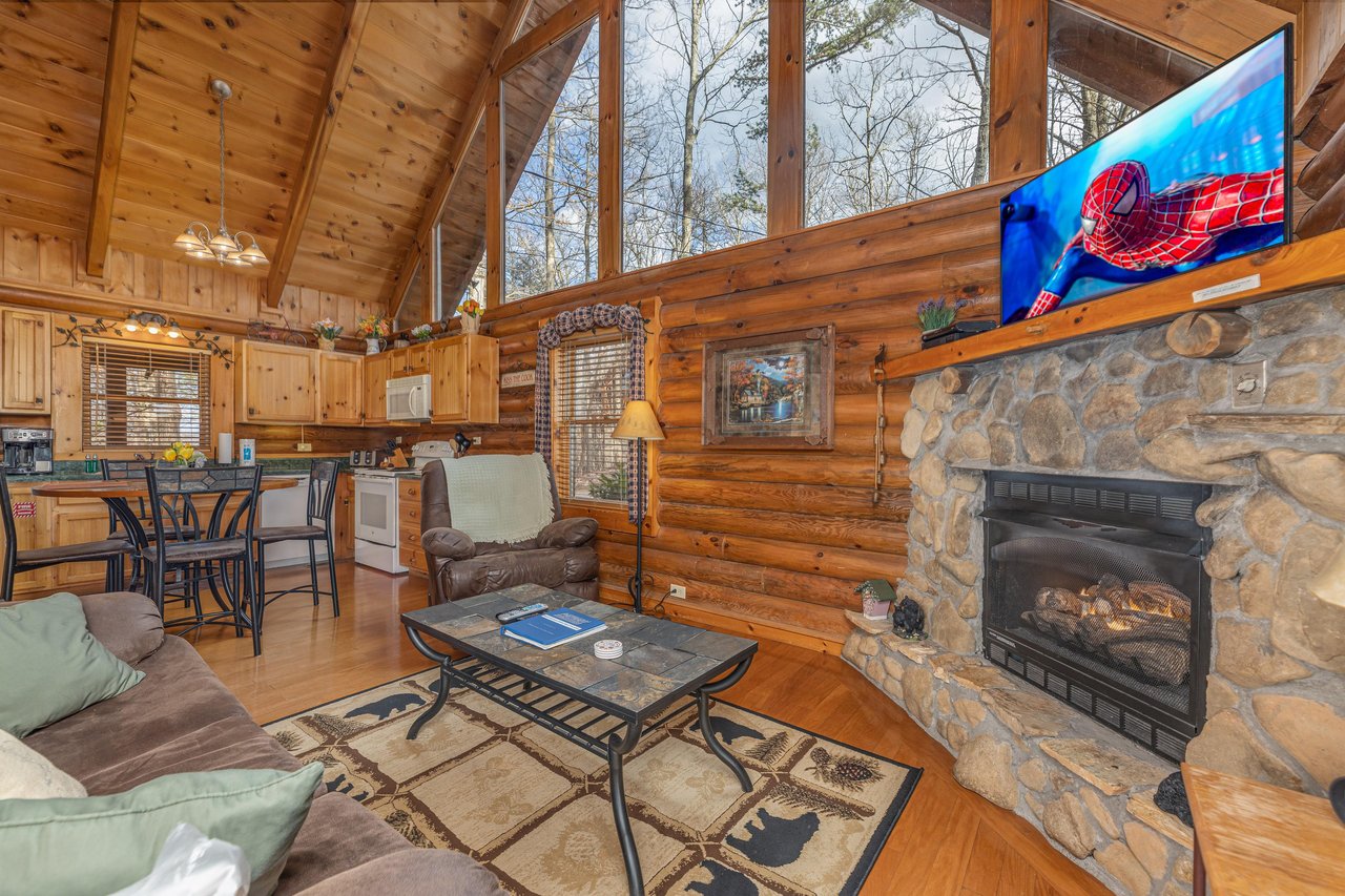 Living room with fireplace and TV attached to a dining space and kitchen at A Lovers Secret, a 1 bedroom cabin rental located in Gatlinburg