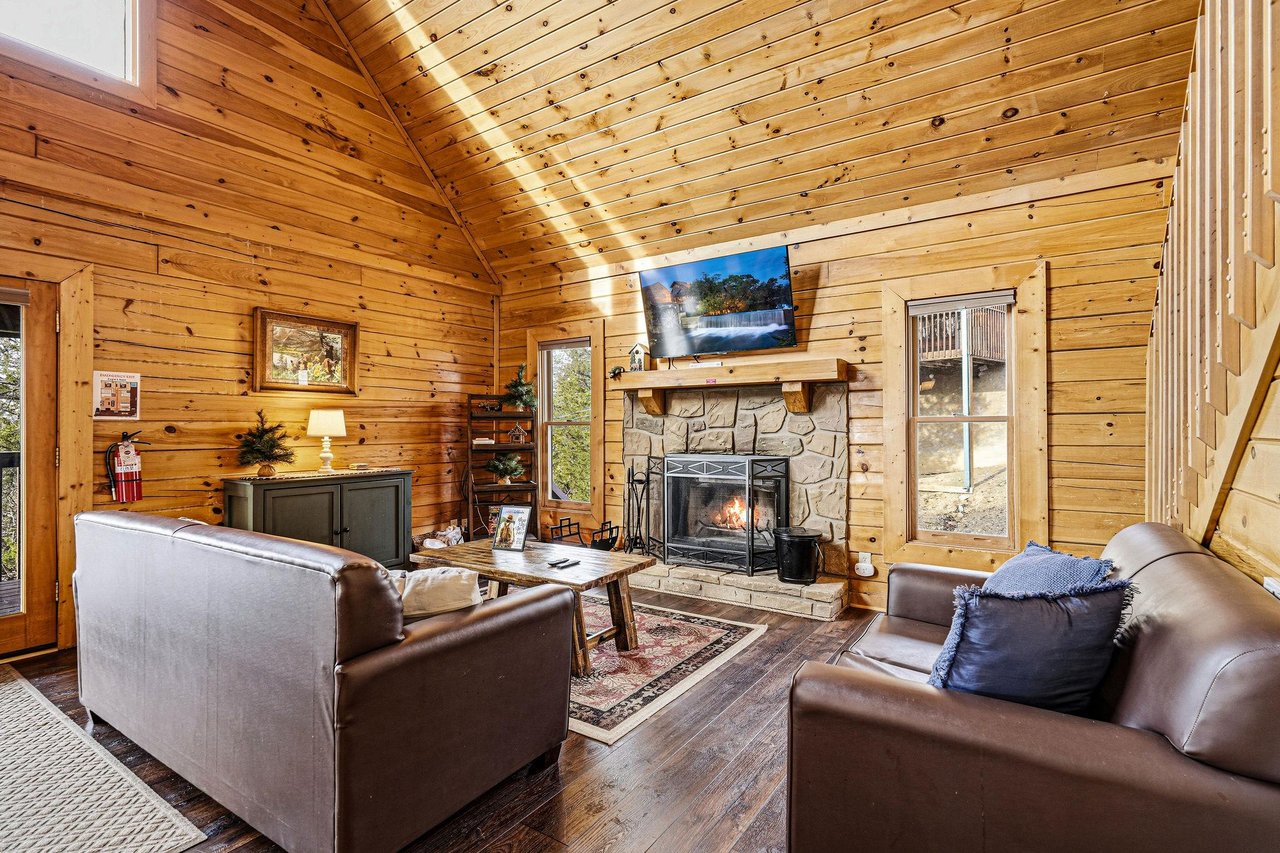 Relax in your cozy cabin living room with warm wood walls, crackling fireplace, and comfortable leather seating for memorable evenings.