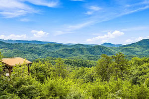 Panoramic mountain vistas stretch endlessly across lush forested peaks beneath a brilliant blue sky, offering a breathtaking natural backdrop to your stay.