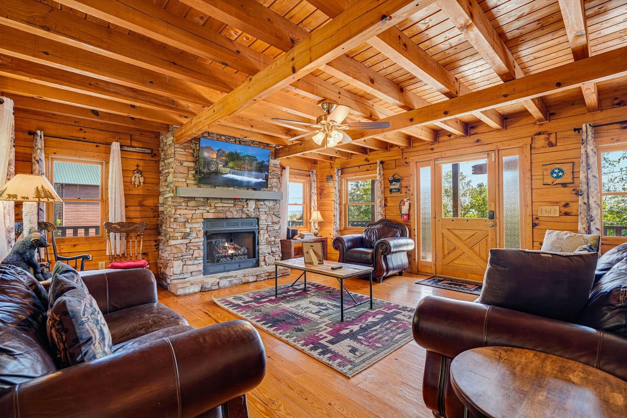 Sink into plush leather sofas in this welcoming living room, where a crackling stone fireplace and towering timber beams create the perfect mountain retreat for your evenings together.