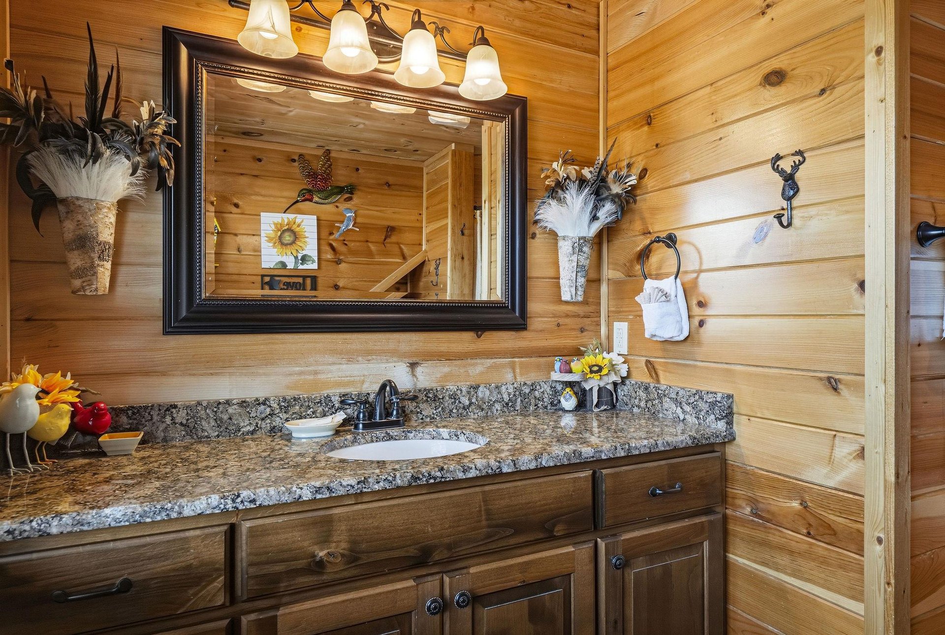 Youll love the rustic charm of this bathroom with warm wood paneling, granite countertops, and playful country décor—perfect for freshening up after a day of adventure.