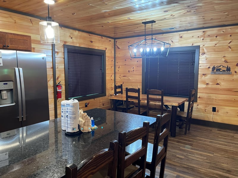 Step into your cozy cabin kitchen and dining area, where rustic wood paneling meets modern convenience. Gather around the solid wood table for meals, and enjoy the warmth of an inviting mountain retre
