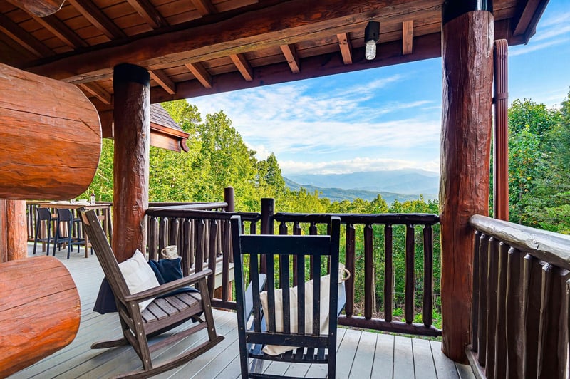 Stunning mountain panorama visible from this covered deck featuring rustic log beams and comfortable rocking chairs—perfect for morning coffee or evening relaxation.