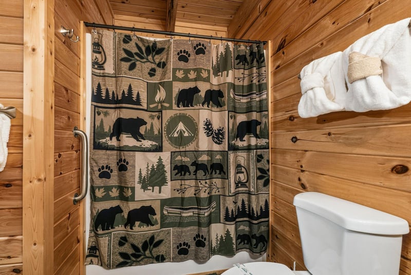 Rustic charm meets woodland whimsy in your cozy bathroom, where warm pine walls and a natureinspired bearandforest shower curtain create a mountain retreat feel. Fresh towels await your arrival.