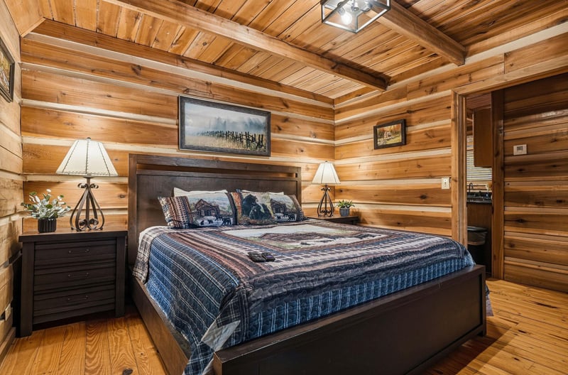 Wrap yourself in rustic warmth beneath soaring wood beams and soft lamplight—your cozy mountain retreat awaits with a plush bed and authentic cabin charm.