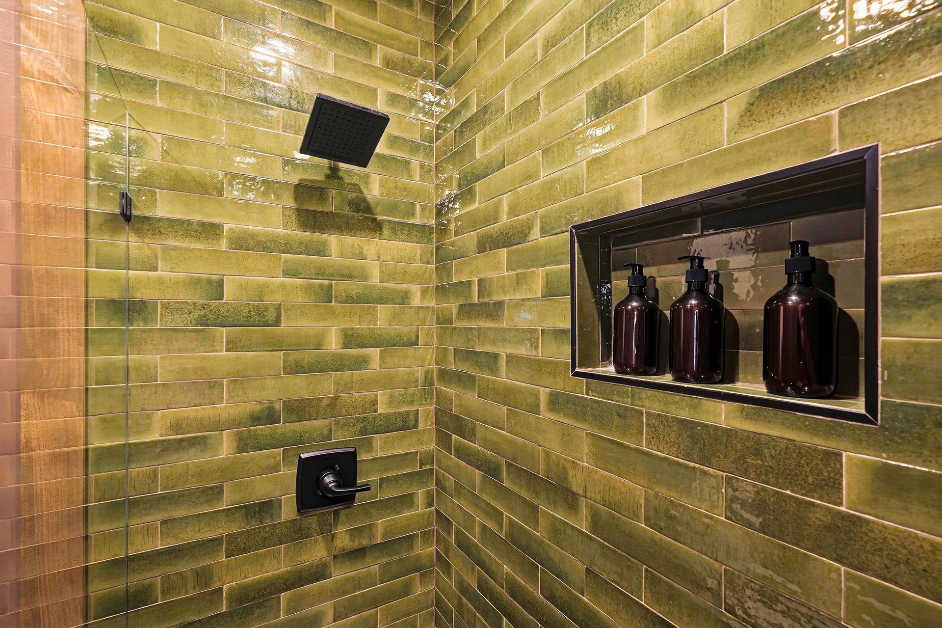 Step into this beautifully tiled shower with sleek green subway tiles, a modern rainfall showerhead, and luxury bath amenities waiting for you.