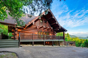 A handcrafted log cabin framed by lush greenery, showcasing rustic wood detailing and a welcoming deck that overlooks the surrounding mountains—the perfect mountain retreat.
