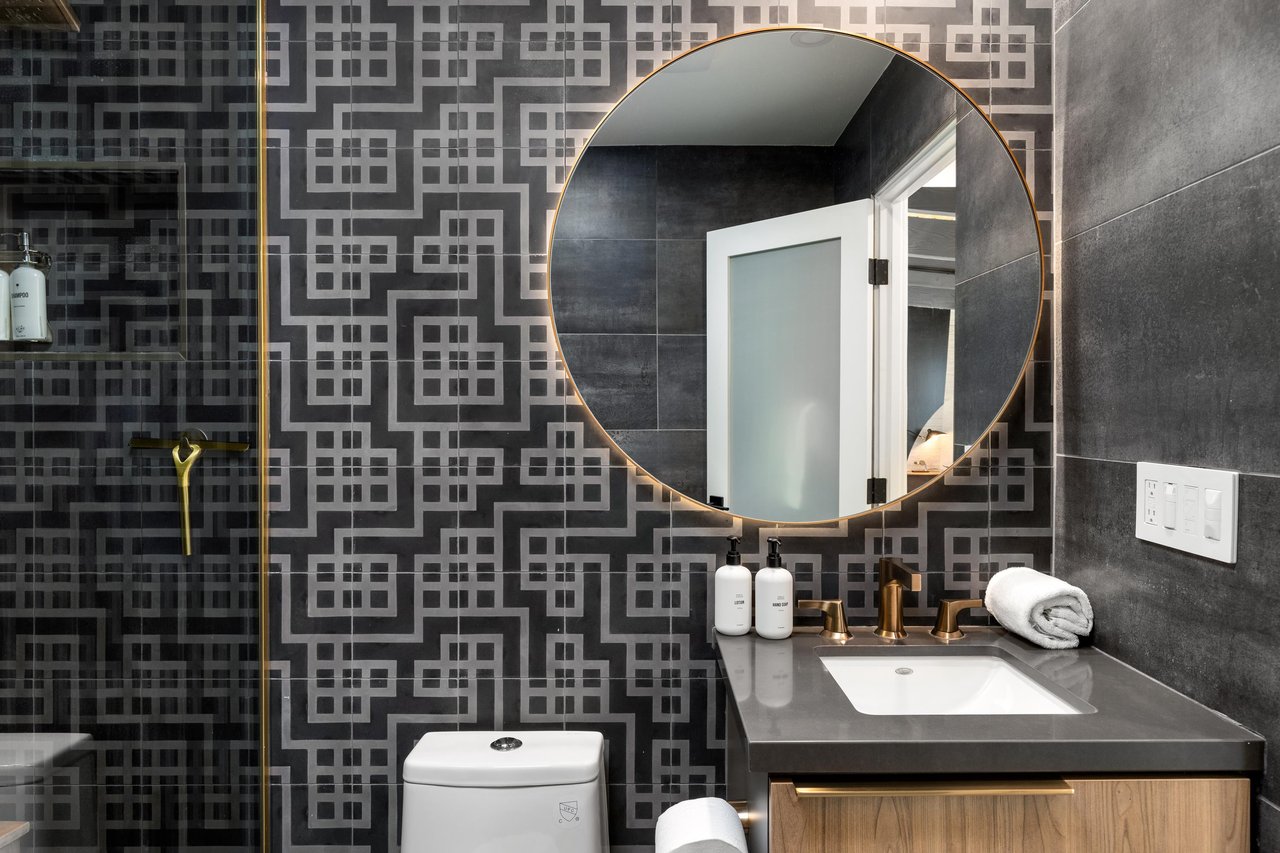 Step into your stylish bathroom featuring modern geometric tiles, brass fixtures, and premium amenities for your refreshing morning routine.