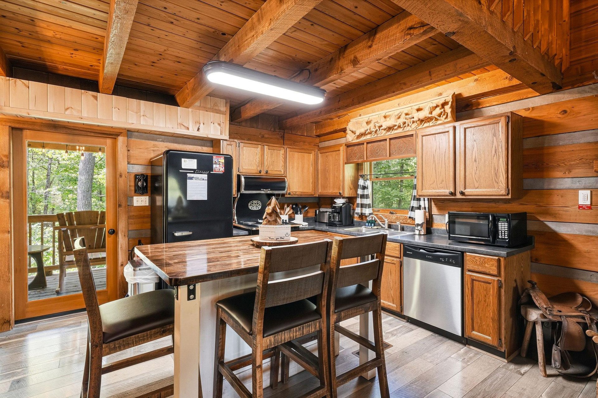 Step into your fully equipped cabin kitchen with warm wood beams, modern appliances, and a charming island where you can share meals with forest views just beyond the door.