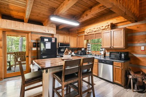 Step into your fully equipped cabin kitchen with warm wood beams, modern appliances, and a charming island where you can share meals with forest views just beyond the door.