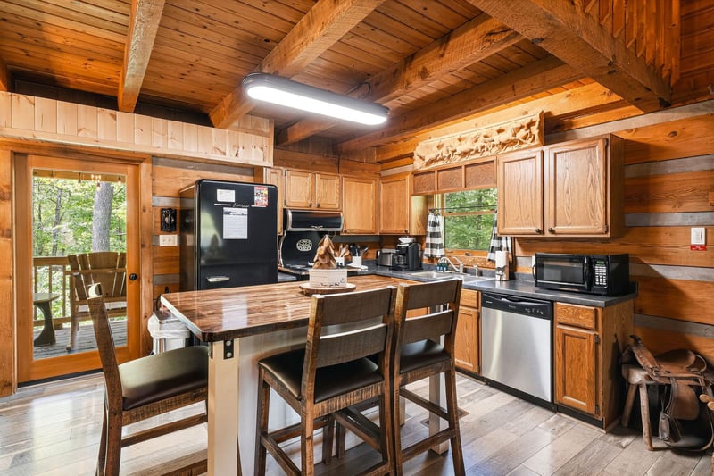 Step into your fully equipped cabin kitchen with warm wood beams, modern appliances, and a charming island where you can share meals with forest views just beyond the door.