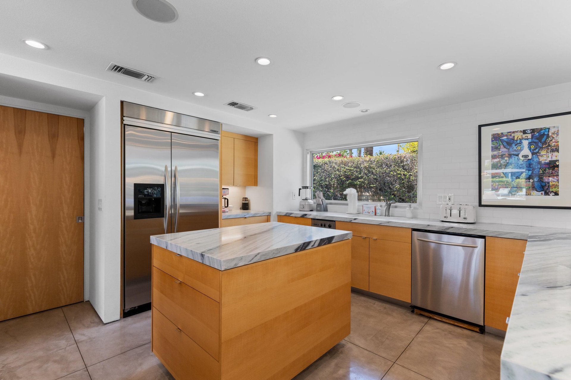Modern chefs kitchen with a waterfall marble counter, kitchen island, stainlesssteel appliances, wine fridge, wet bar, and kitchen essentials.