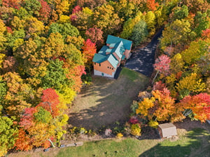 Aerial view of this secluded property surrounded by vibrant autumn foliage in reds, golds, and greens with private driveway and outbuilding.