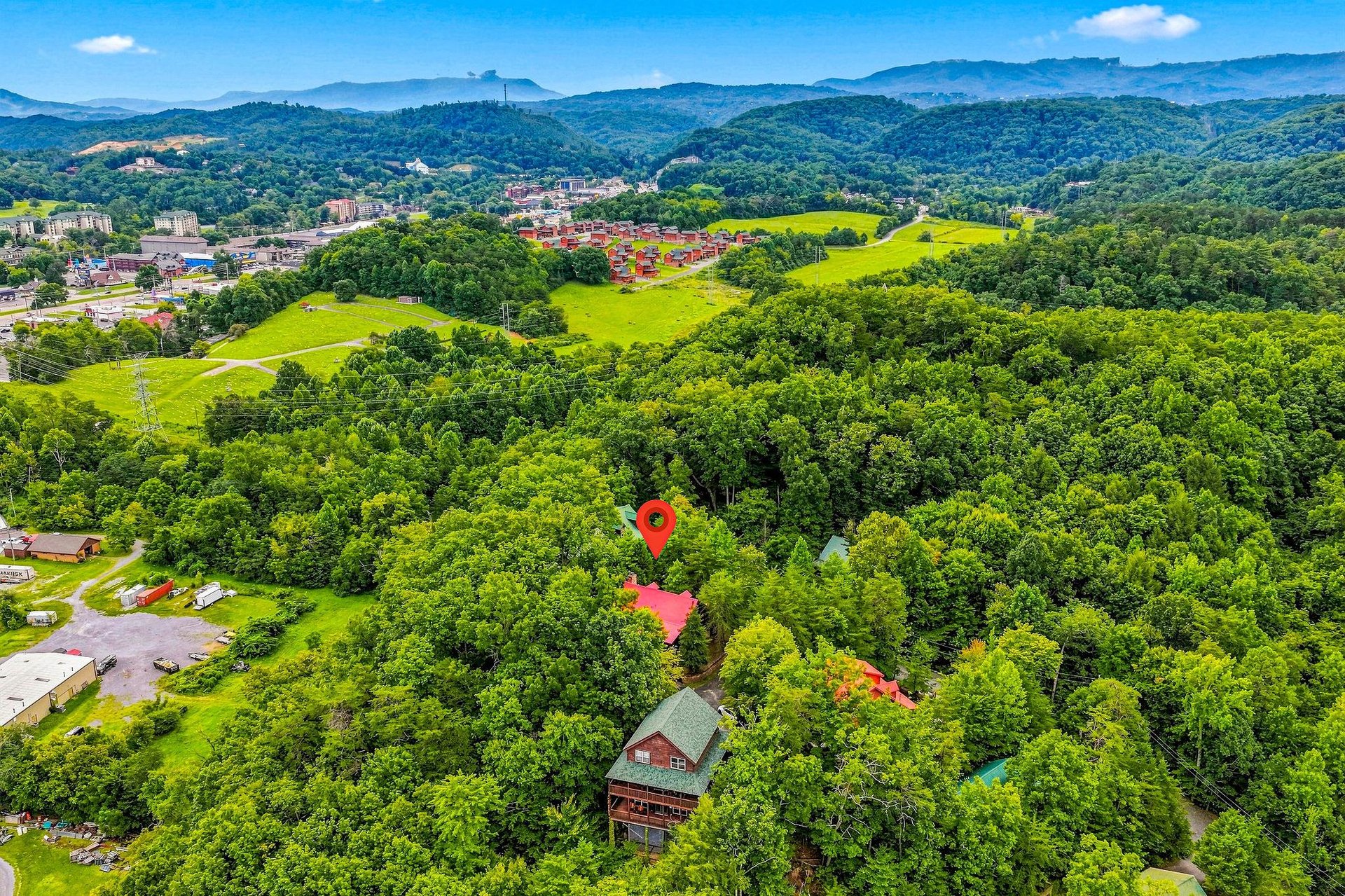 This aerial view showcases the propertys serene, wooded setting with rolling hills and nearby mountain vistas, offering a peaceful retreat close to area attractions.