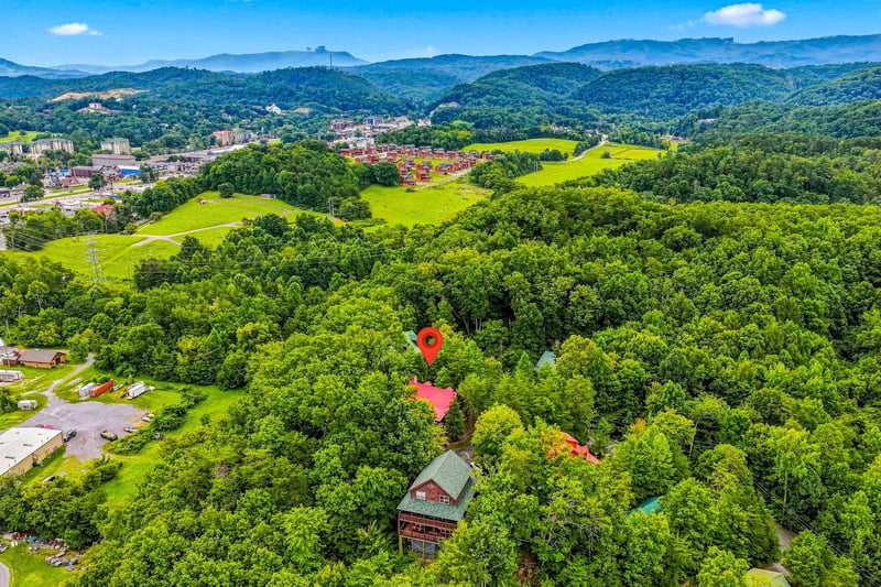 This aerial view showcases the propertys serene, wooded setting with rolling hills and nearby mountain vistas, offering a peaceful retreat close to area attractions.