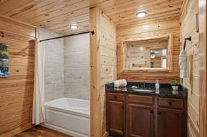 Warm woodpaneled bathroom offers a welcoming blend of comfort and style. Crisp white tub and fresh towels await, while a rustic mirror and sleek countertops create your perfect space to unwind.