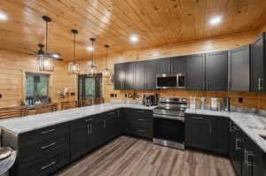 Your fully equipped kitchen awaits with sleek dark cabinetry, granite countertops, and rustic wood ceilings that create the perfect mountain retreat atmosphere.
