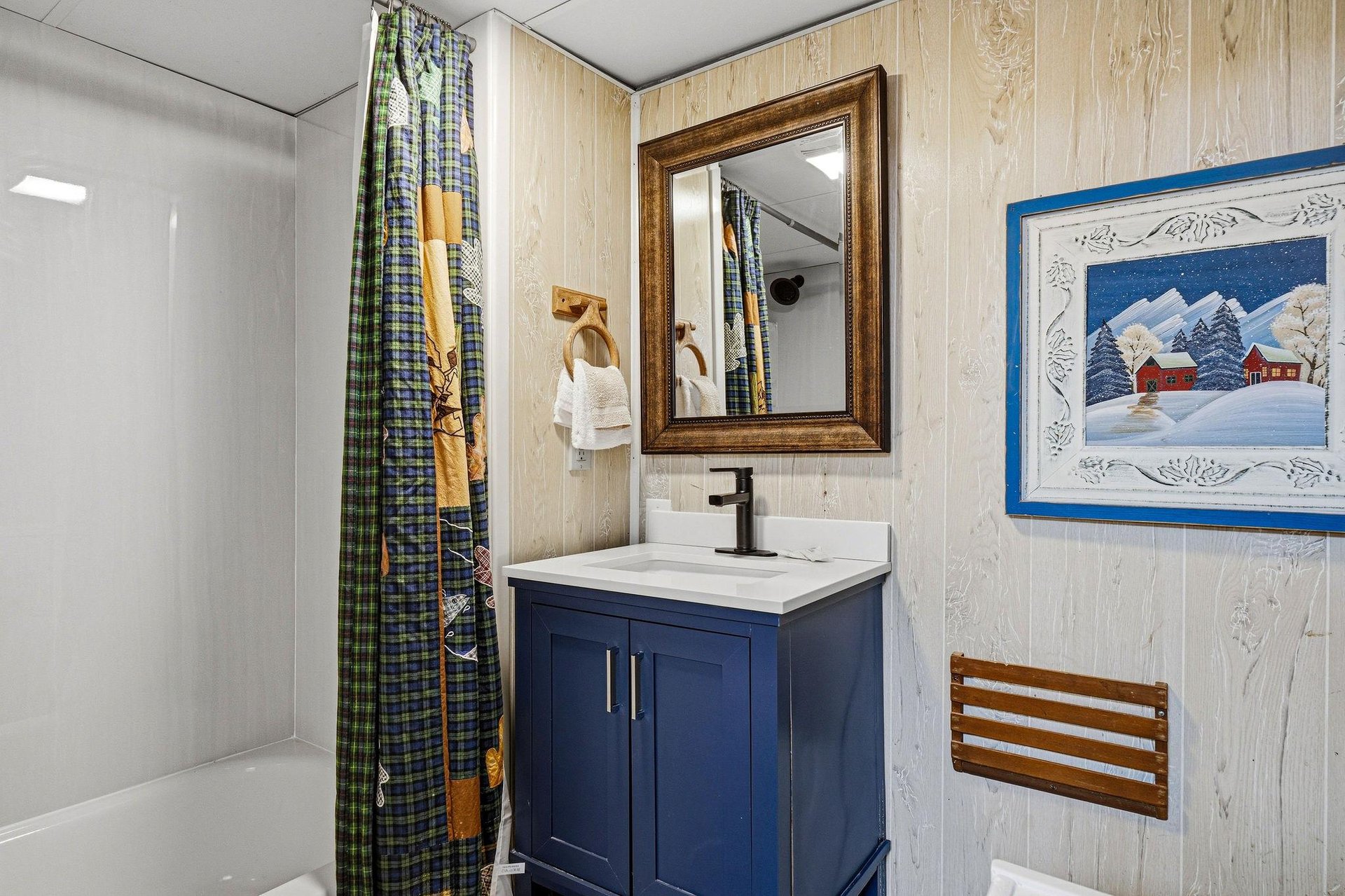 Step into your refreshing bathroom, complete with a nauticalblue vanity and warm whitewashed wood walls. Ski gear and fishing rods hang ready for your mountain adventures, while charming cabin décor 