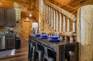 Step inside your rustic cabin retreat where natural wood beams and a stunning log staircase create mountain charm. Your dining area awaits with vibrant blue accents and cozy seating for memorable meal