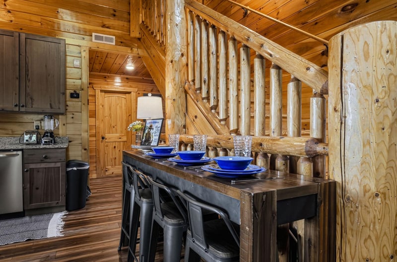 Step inside your rustic cabin retreat where natural wood beams and a stunning log staircase create mountain charm. Your dining area awaits with vibrant blue accents and cozy seating for memorable meal