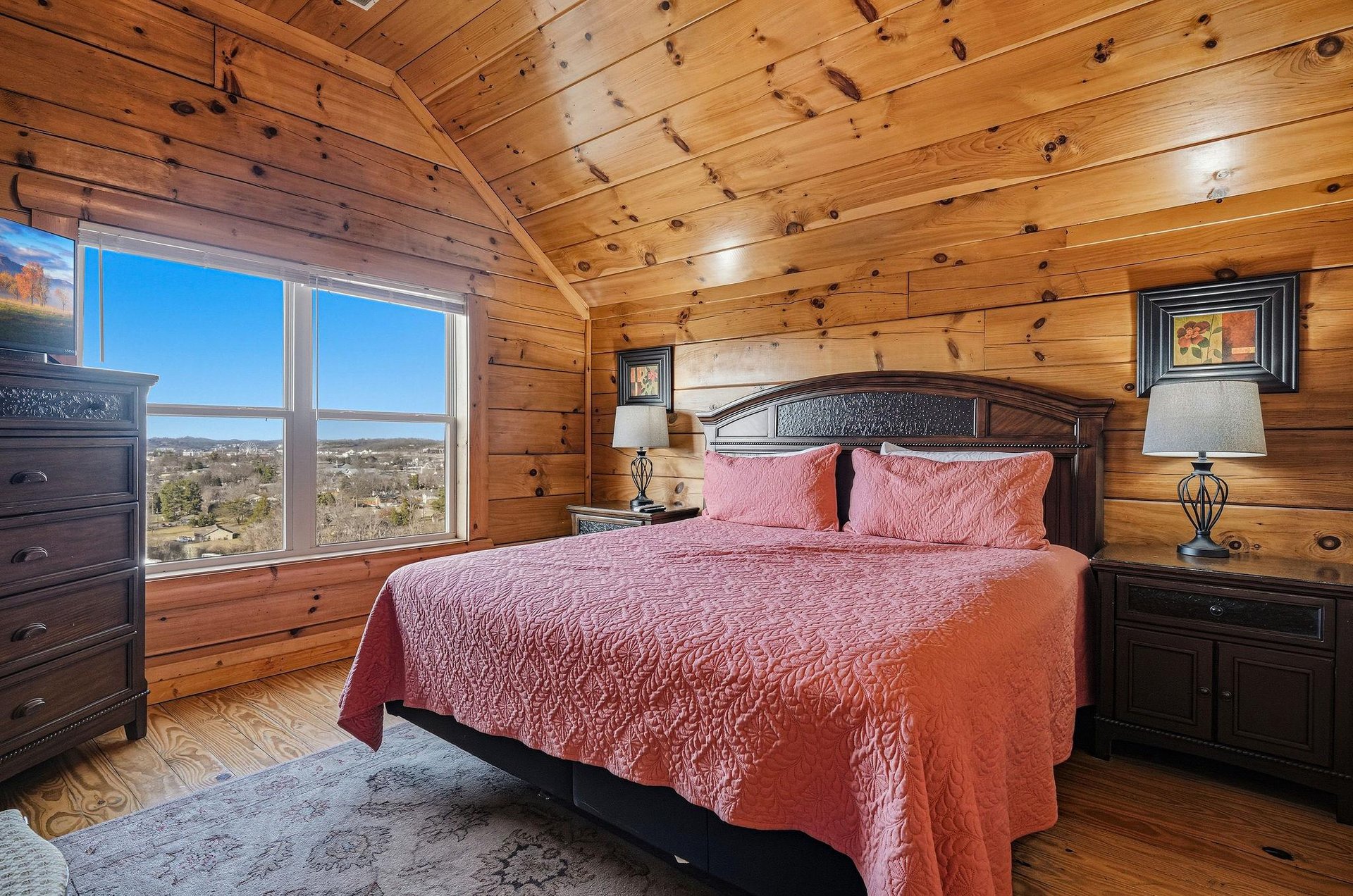 Cozy woodpaneled bedroom with plush bedding and stunning landscape views through large windows for restful mountain mornings.