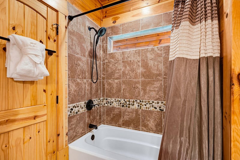 Refresh after your adventures in this tiled tubshower combo featuring a handheld showerhead, decorative stone accent strip, and plush towels waiting for you on the door.