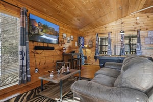 Cozy up in your rustic living room with warm wood walls, plush seating, and entertainment for memorable mountain evenings.