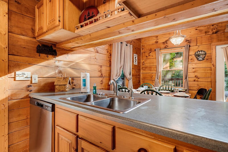 Warm wood surrounds you in this cozy cabin kitchen with everything you need to whip up meals, from the dishwasher to the bright window framing lush greenery outside.