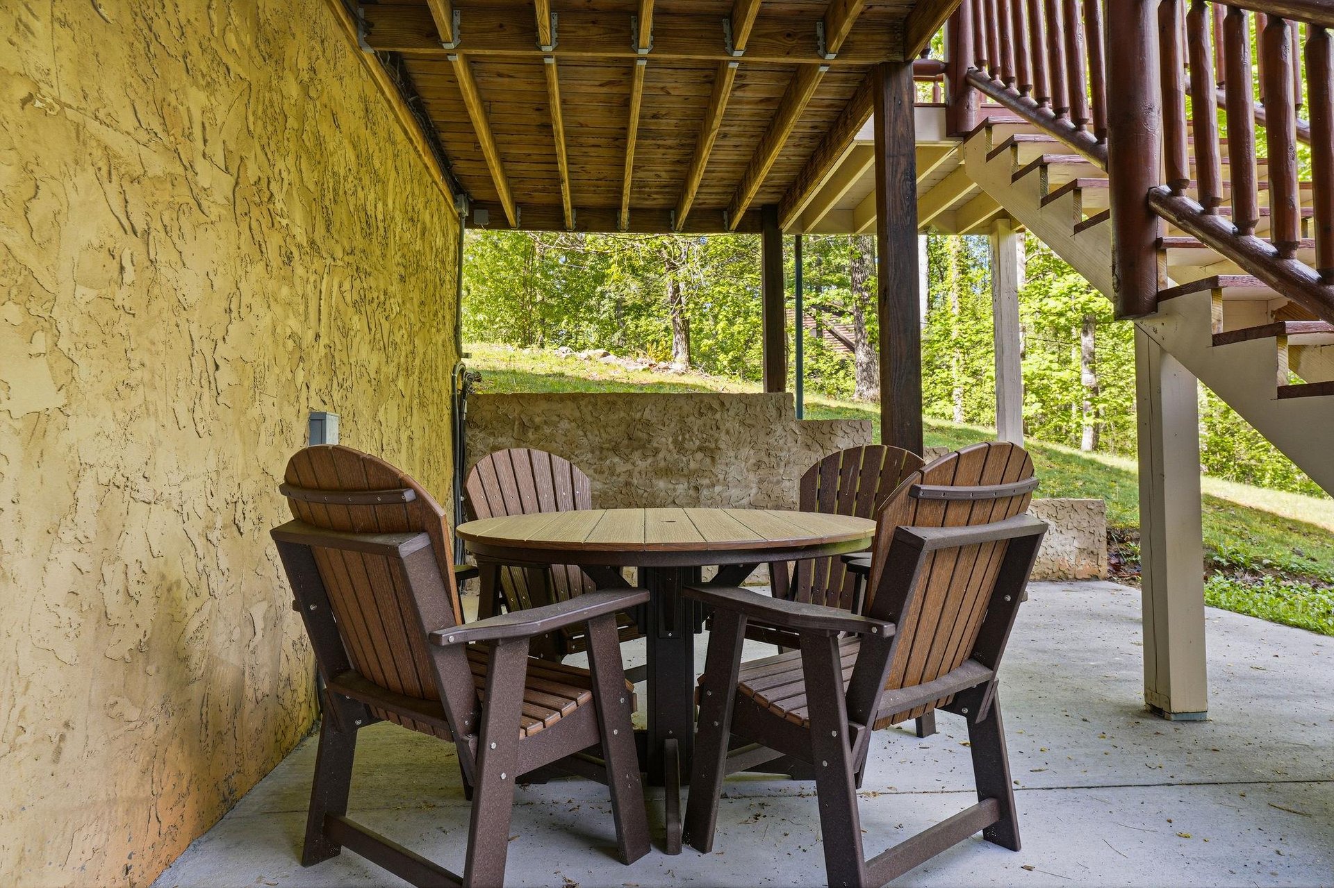 Unwind on your covered patio with comfortable seating for outdoor meals and relaxation, surrounded by natural greenery and stone details.