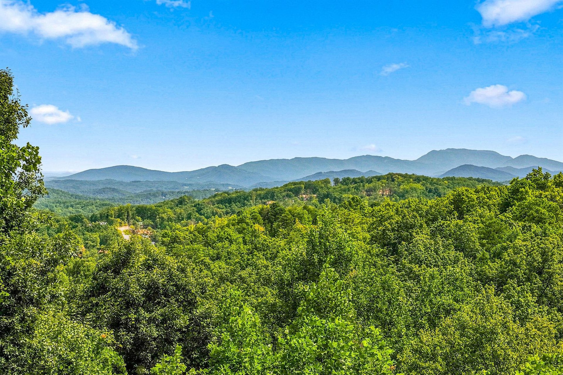 A stunning panorama of layered mountain ridges stretches across the horizon, framed by lush summer forest—an inspiring backdrop to your mountain retreat.
