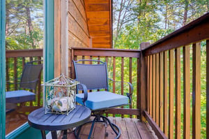Unwind on your own private balcony surrounded by lush forest. Two comfy chairs and a cozy table await your morning coffee or evening relaxation, with sunlight filtering through the trees.