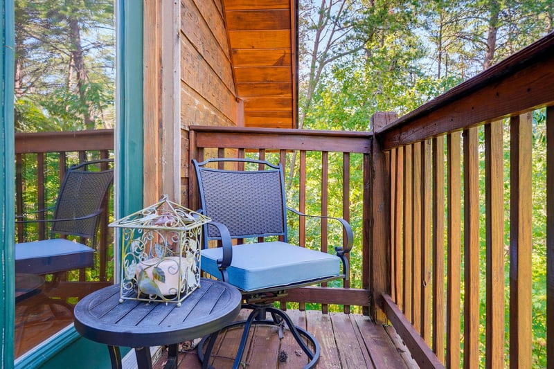 Unwind on your own private balcony surrounded by lush forest. Two comfy chairs and a cozy table await your morning coffee or evening relaxation, with sunlight filtering through the trees.