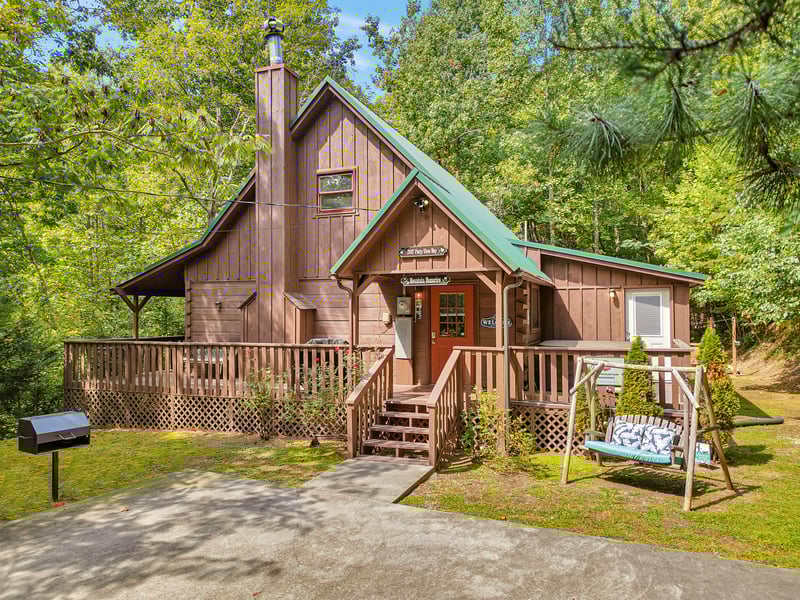 Charming cabin nestled among towering trees offers rustic charm with modern comforts, featuring a welcoming front porch and peaceful forest surroundings.