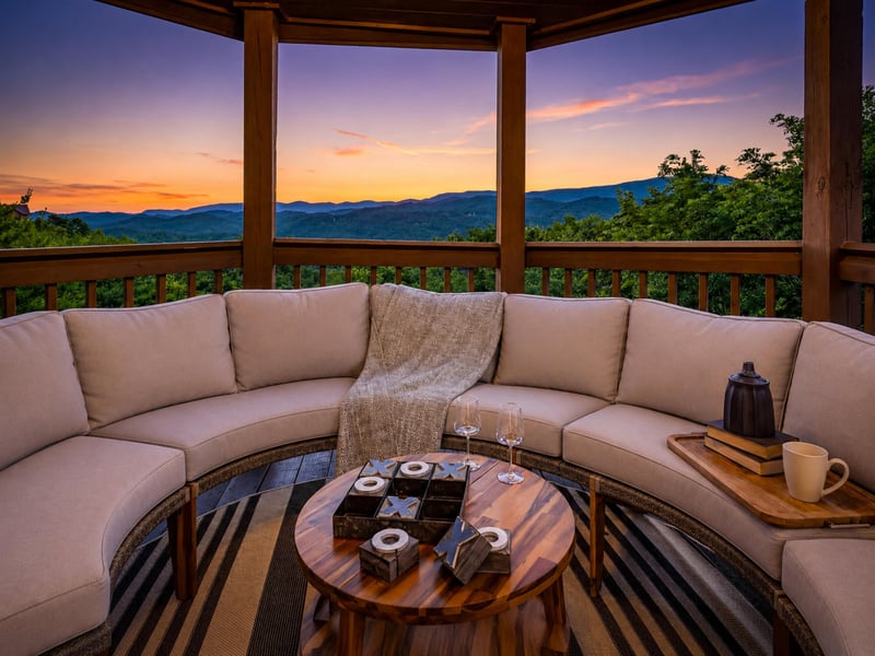 A covered deck frames breathtaking mountain views at sunset, with a curved sofa and gameready table inviting relaxation amid the vibrant evening sky.