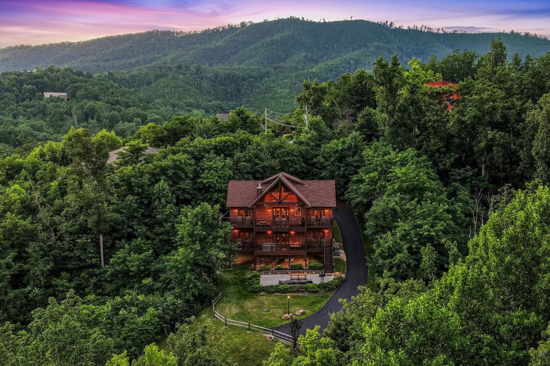 Aerial view of a secluded log cabin nestled in lush forested mountains at dusk, showcasing the propertys private natural setting and scenic landscape.