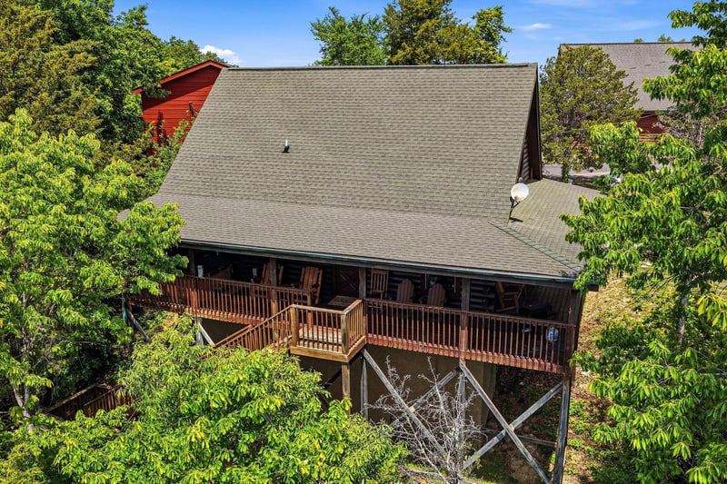 Elevated mountain cabin nestled among lush trees, featuring spacious wraparound deck and peaceful wooded surroundings—a serene retreat perched above the landscape.