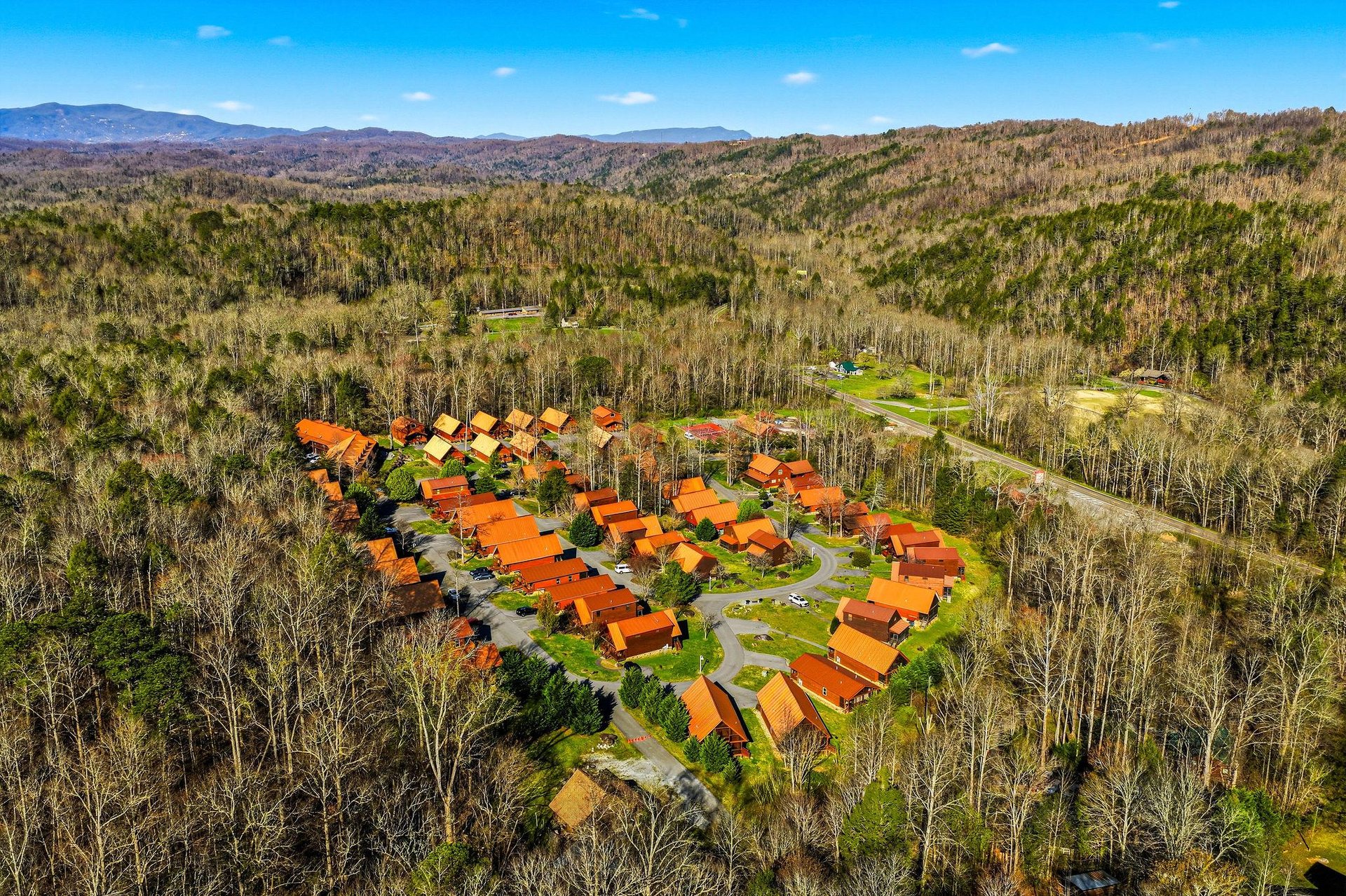 Aerial view of a rustic cabin resort nestled in pristine wilderness, surrounded by rolling mountains and endless forest views.