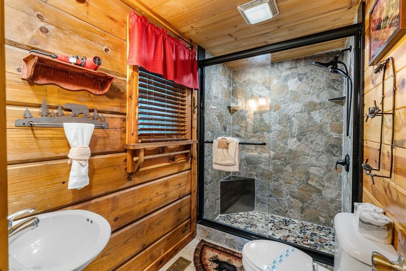 Full bathroom with pedestal sink and walk in shower with stone wall
