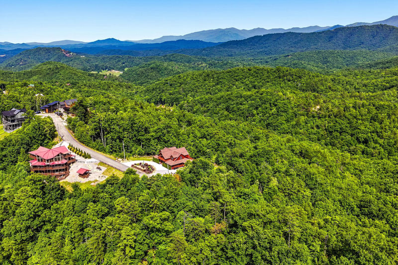 Aerial view of mountain vacation properties nestled in lush forested hills, with sweeping views of layered mountain ranges stretching toward the horizon.