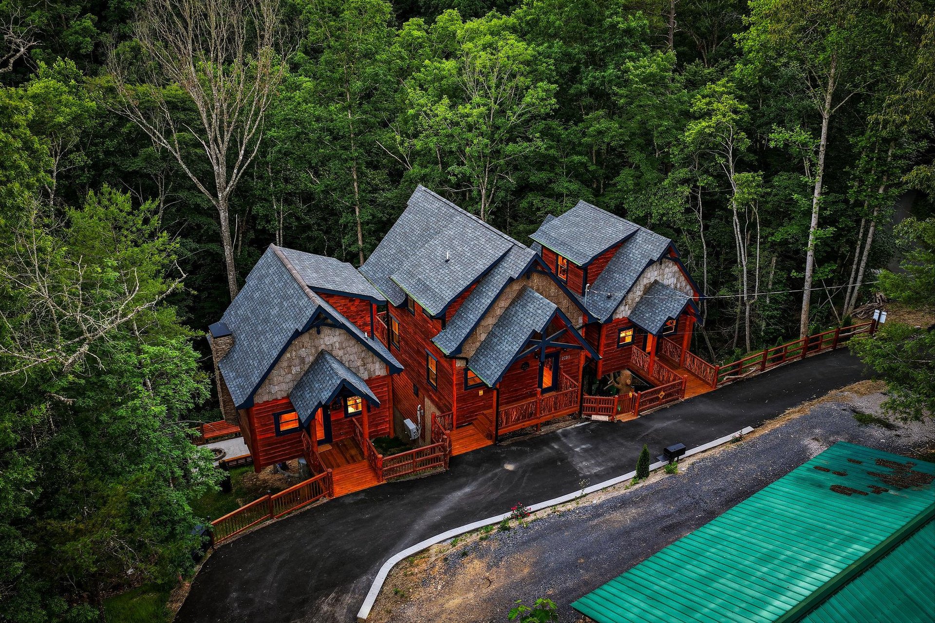 Aerial view of distinctive multiunit mountain cabin structures nestled among dense forest, featuring rich wood exteriors, steep shingled roofs, and wraparound decks.