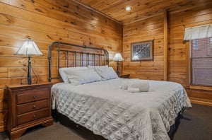 Sink into soft linens and drift off under the warm glow of rustic wood paneling. Your peaceful cabin bedroom awaits with charming ironframed comfort and cozy bedside lighting.
