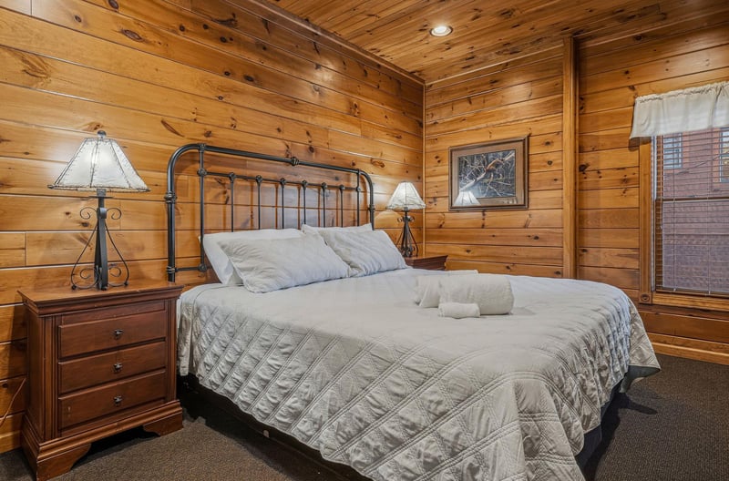 Sink into soft linens and drift off under the warm glow of rustic wood paneling. Your peaceful cabin bedroom awaits with charming ironframed comfort and cozy bedside lighting.