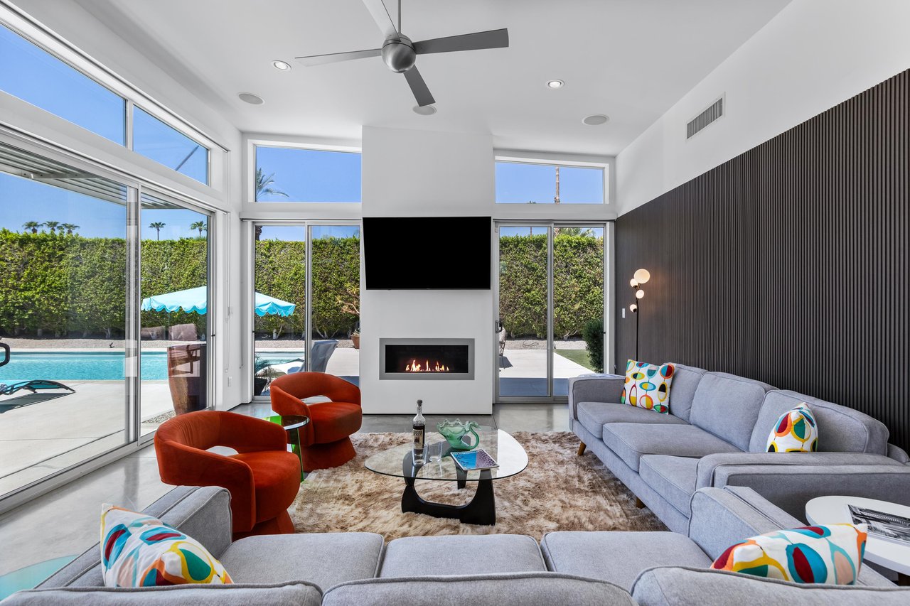 Modern living room with ample seating, gas fireplace, flatscreen TV, patio access, poolspa views, and plenty of natural lighting.