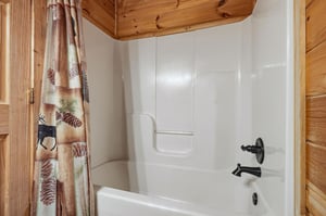 Your cozy cabin bathroom features a deep soaking tub perfect for unwinding after mountain adventures, complete with charming pine cone curtains.
