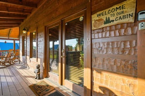 Step onto your private covered porch where rocking chairs and rustic mountain charm await. The welcoming cabin entrance sets the tone for a cozy, unforgettable retreat.