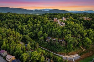 Aerial view capturing the property nestled among lush forests with mountain ridges stretching across the horizon at dusk, showcasing the scenic natural surroundings and secluded setting of the area.